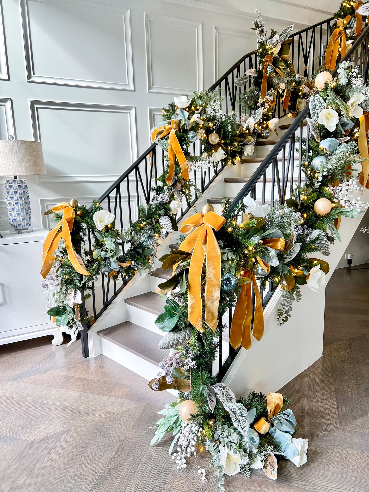 Green and silk floral garland wraps around staircase metal handrail with yellow ribbons