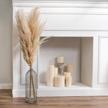 Neutral stem in vase next to white fireplace filled with cream unlit candles