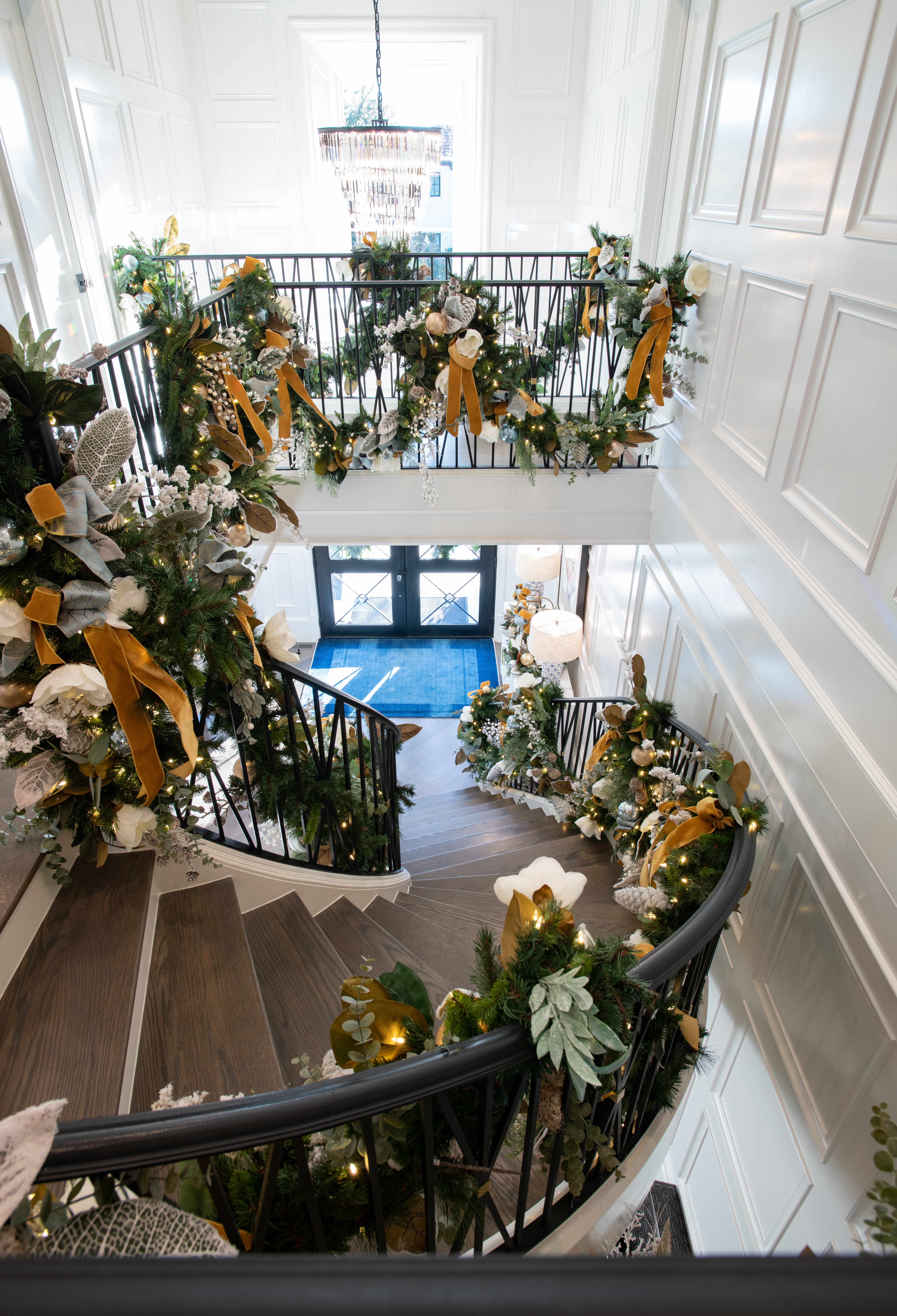 Curved staircase adorned with garland and yellow ribbon descends to home entryway