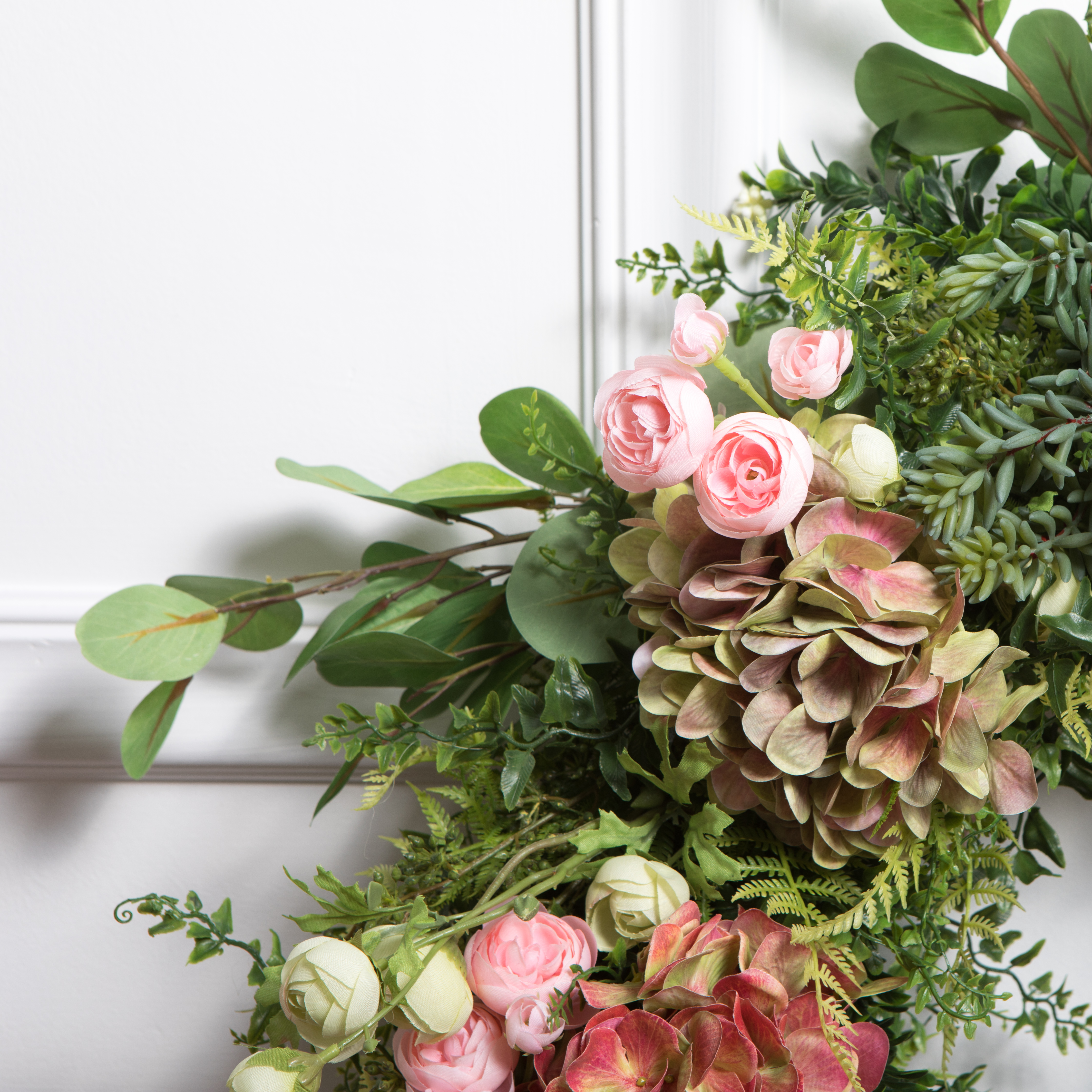 Faux florals and faux greenery arranged into wreath on white door background